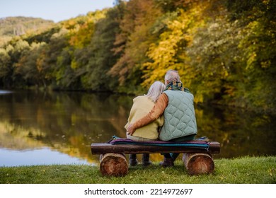 Senior couple in love sitting together on bench looking at lake, during autumn day. Rear view. - Shutterstock ID 2214972697