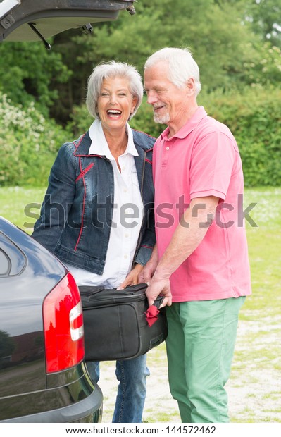 Senior couple with\
luggage at a black car
