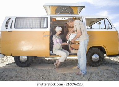 Senior Couple Making Tea In Camper Van On Beach