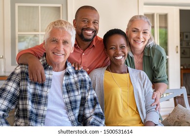 Senior Couple With Mature Man And African Woman Posing For A Photo Sitting At Courtyard. Portrait Of Happy Multiethnic People On Couch Outdoor. Cheerful Men And Beautiful Women Looking At Camera.