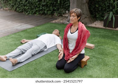 Senior couple meditating together on yoga mats and wooden stool in peaceful scene showcasing the art of relaxation within a tranquil home garden environment. Copy space, full length . Horizontal - Powered by Shutterstock