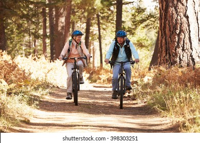 Senior Couple Mountain Biking On Forest Trail, California