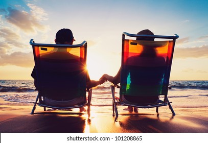 Senior Couple Of Old Man And Woman Sitting On The Beach Watching Sunset