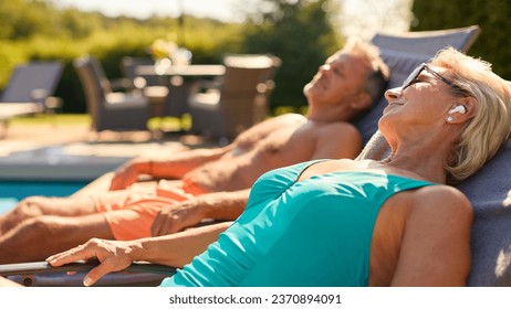 Senior Couple On Holiday With Woman Wearing Wireless Earbuds By Hotel Swimming Pool - Powered by Shutterstock