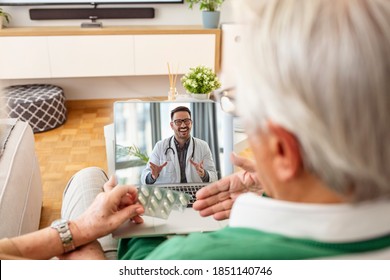 Senior Couple On Online Therapy. They Are Sitting On The Sofa, Having A Video Call With A Doctor. Senior Couple Consulting With Their Doctor. Health Care And Modern Technology For The Elderly.