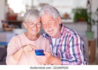 Senior Couple On Video Call Via Mobile Phone. Joyful And Smiling Beautiful Elderly Couple Sitting At Home Being In Great Mood Holding Smartphone