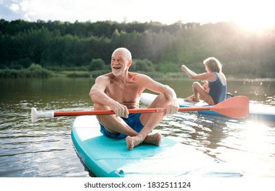 Senior Couple Paddleboarding On Lake In Summer.