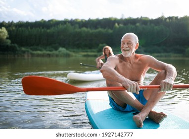 Senior couple paddleboarding on lake in summer.
