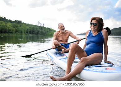 Senior Couple Paddleboarding On Lake In Summer.