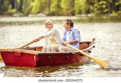 Senior Couple Paddling On Boat On Mountain Tarn