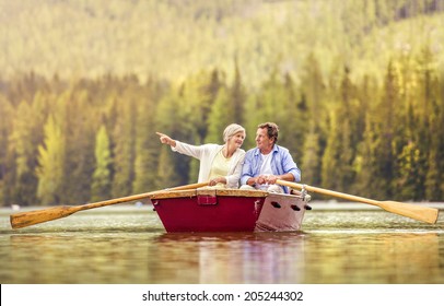 Senior Couple Paddling On Boat With Mountains In Background