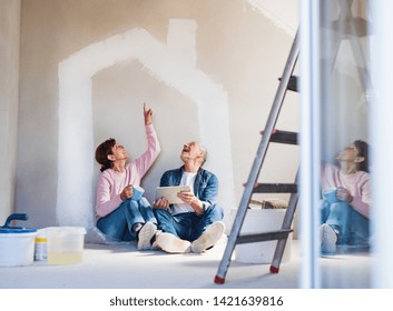 Senior couple painting walls in new home, using tablet. Relocation concept. - Powered by Shutterstock