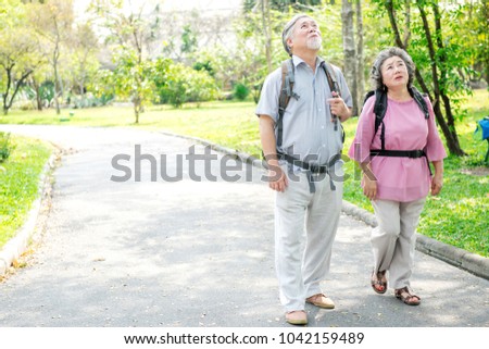 Senior couple in park walking with backpack. Chinese old couple in park, relaxing, smiling. With copy space.