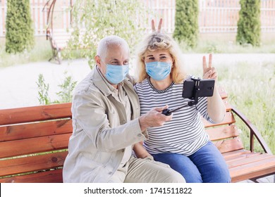 Senior couple in the park wearing medical mask to protect from coronavirus and making selfie in spring or summer day, coronavirus quarantine - Powered by Shutterstock