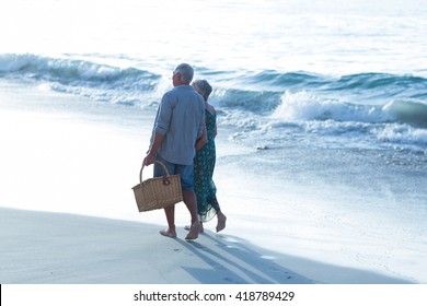 Senior Couple With A Picnic Basket At The Beach