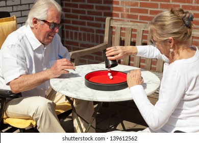 Senior Couple Playing Dice Game Outdoor In Garden. Yahtzee.