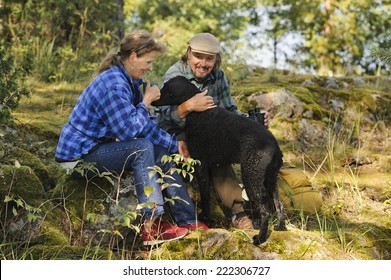 Senior Couple Playing With Their Pet Dog While Out Hiking. The Dog Is A Curly Haired Retriever.Focus Is On Woman