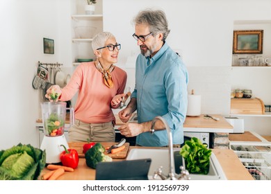 Senior couple preparing healthy smoothie in kitchen and using tablet to read recipe - Shutterstock ID 1912569739