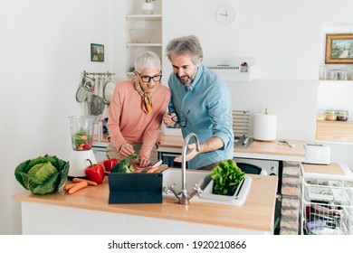 Senior couple preparing healthy smoothie in kitchen and using tablet to read recipe - Shutterstock ID 1920210866