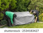 Senior couple put garden seat cover onto outdoor furniture bench set in home backyard garden ready for winter