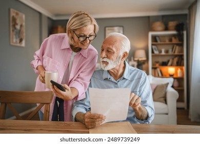 senior couple read a document from envelope and use cellphone together - Powered by Shutterstock