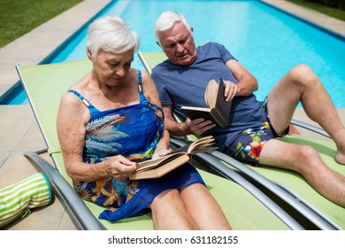 Senior couple reading books on lounge chair at poolside - Powered by Shutterstock