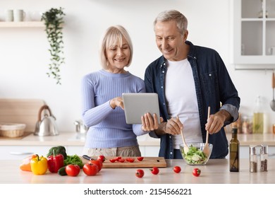 Senior couple reading food blog on digital tablet, cooking together healthy vegetable salad at home kitchen, happy mature man and woman making lunch, checking nice recipes on Internet - Powered by Shutterstock