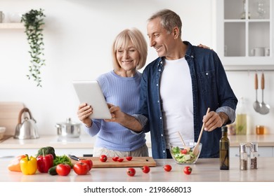 Senior Couple Reading Food Blog On Digital Tablet, Cooking Together Healthy Vegetable Salad At Home, Happy Mature Man And Woman Making Lunch, Checking Nice Recipes On Internet, Copy Space