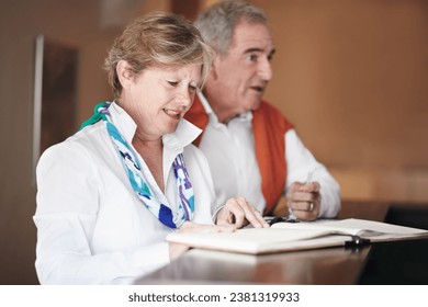 Senior couple, reading and signing documents at hotel reception desk for booking, reservation or vacation. Mature man and woman filling forms, application or checking paperwork or sign in at resort - Powered by Shutterstock