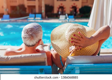 Senior Couple Relaxing By Swimming Pool Lying On Chaise-longues. People Enjoying Summer Vacation.