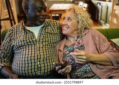 Senior couple relaxing on couch while using smartphone and remote control - Powered by Shutterstock