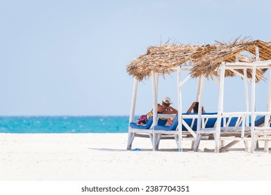 Senior couple relaxing on deck chairs at the beach.White sandy beach and turquoise ocean,luxury beach house. - Powered by Shutterstock