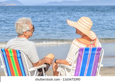 Senior couple relaxing and talking on beach in chair