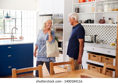 Senior Couple Returning Home From Shopping Trip Carrying Grocery Bags Through Kitchen