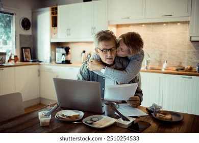 Senior couple reviewing bills together at home in the kitchen - Powered by Shutterstock