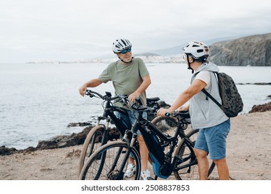 Senior couple riding bikes together in rocky beach enjoying outdoor. Active mature people talking holding mountain bikes. Bicycle lifestyle concept, having fun - Powered by Shutterstock