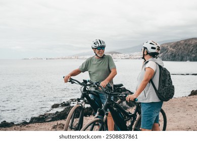 Senior couple riding bikes together in rocky beach enjoying outdoor. Active mature people talking holding mountain bikes. Bicycle lifestyle concept, having fun - Powered by Shutterstock