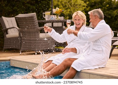 Senior Couple In Robes Outdoors Drinking Champagne By Swimming Pool On Splashing In Water On Spa Day - Powered by Shutterstock