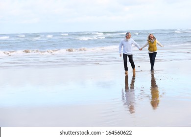 Senior couple running on the beach in winter time