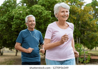 Senior Couple Running Outside At Park. Elderly Man And Old Woman Jogging Together. Retired Man And Active Woman Exercising Outdoor.