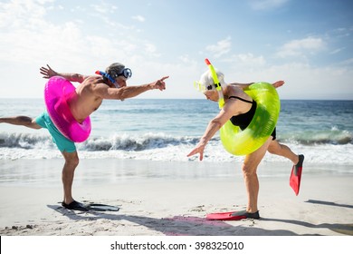 Senior couple with scuba gear and inflatable ring enjoying their holidays on beach