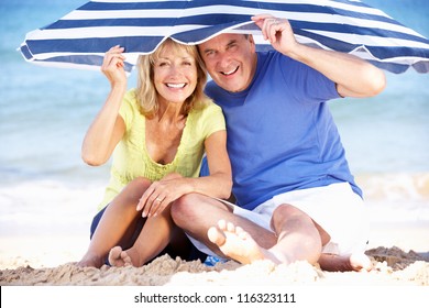 Senior Couple Sheltering From Sun Under Beach Umbrella