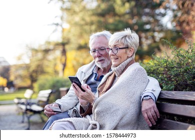 Senior couple shopping on line with mobile phone and credit card while sitting on the bench in park - Powered by Shutterstock