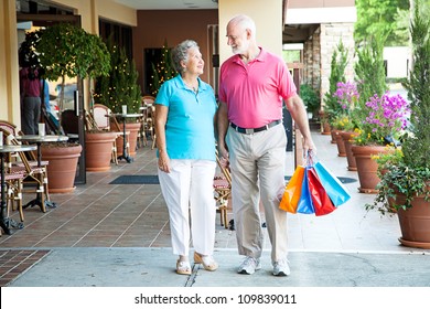 Senior Couple Shopping Together At An Outdoor Mall, Holding Hands.