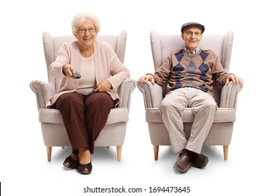 Senior couple sitting in an armchairs and holding a tv remote control isolated on white background