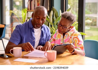 Senior Couple Sitting Around Table At Home Reviewing Finances Using Digital Tablet - Powered by Shutterstock