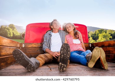 Senior Couple Sitting In Back Of Red Pickup Truck