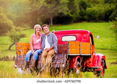 Senior Couple Sitting In Back Of Red Pickup Truck