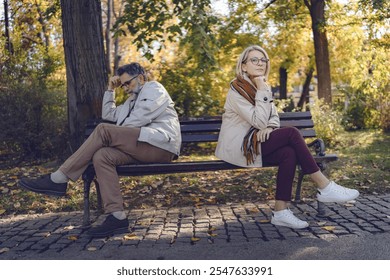 Senior couple sitting back-to-back on a park bench, looking upset and distant, depicting disagreement, relationship challenges, or emotional disconnect in an autumn park setting. - Powered by Shutterstock