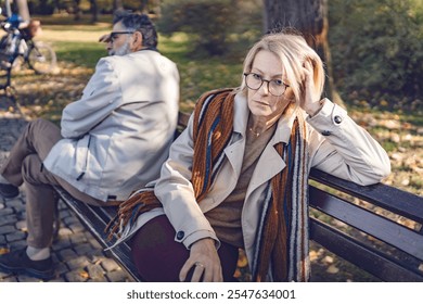 Senior couple sitting back-to-back on a park bench, looking upset and distant, depicting disagreement, relationship challenges, or emotional disconnect in an autumn park setting. - Powered by Shutterstock